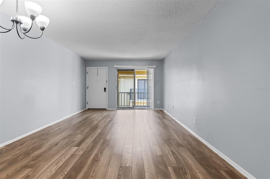An empty living room features light gray walls, wood-look flooring, a ceiling light, and sliding doors — 7612 NACIDO COURT, TAMPA, FL