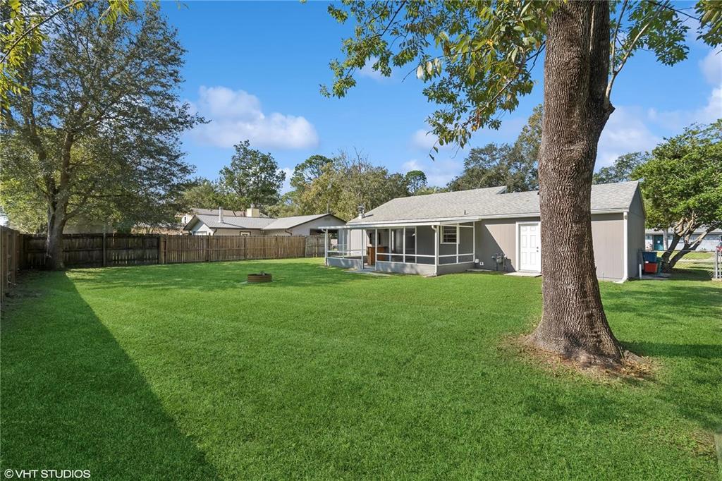 A grassy backyard features a screened-in porch, a fire pit, and a large tree — 2411 NW 54TH AVENUE, GAINESVILLE, FL