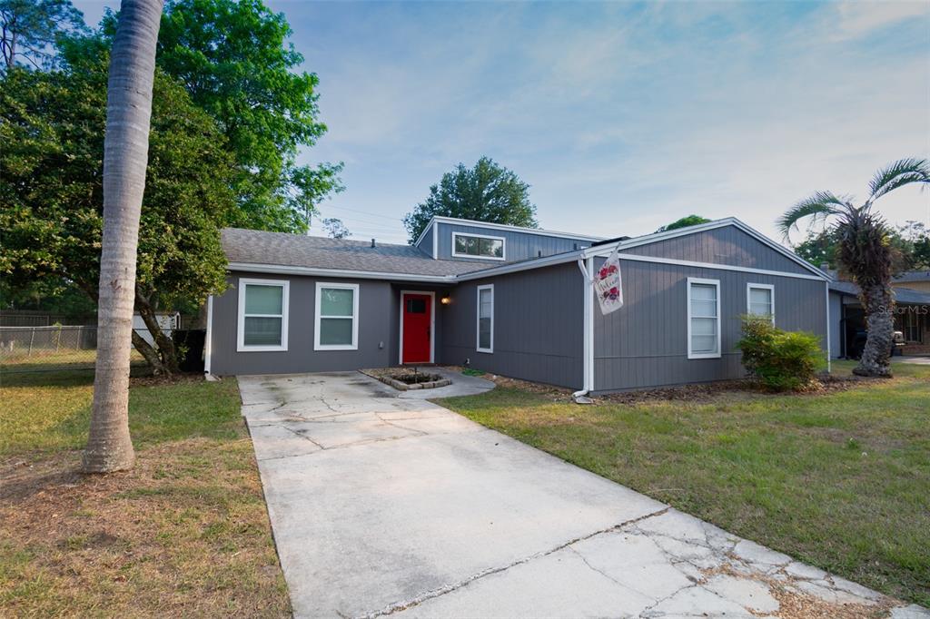 A gray, single-story house with a red front door and a concrete driveway — 2411 NW 54TH AVENUE, GAINESVILLE, FL