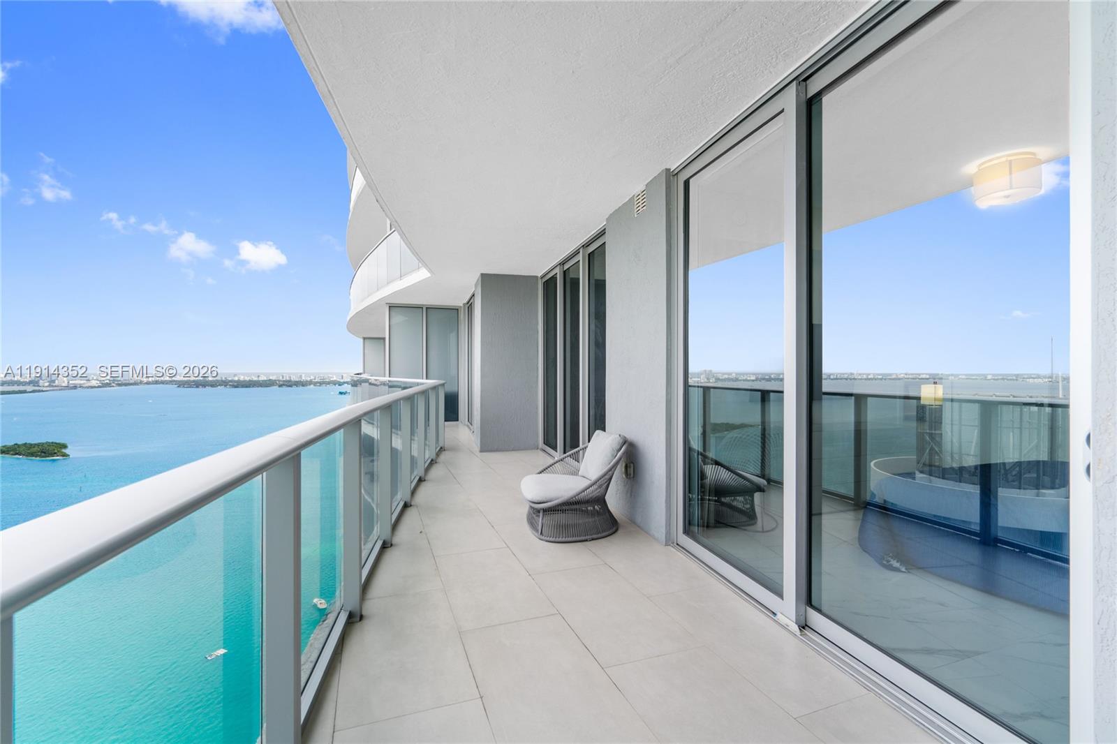 A modern balcony features light tile flooring, a glass railing, and a single wicker chair — 488 NE 18th St # 4309, Miami FL 33132, MIAMI, FL