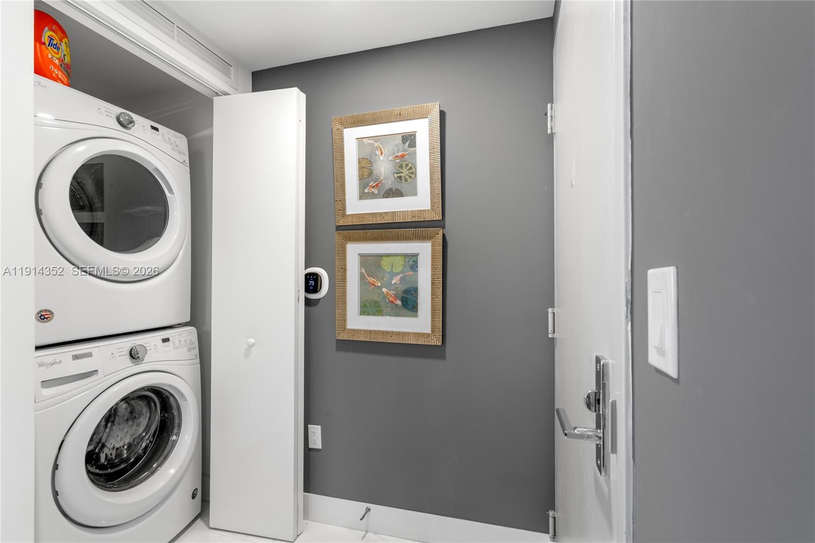 A laundry closet with stacked appliances sits next to a gray wall with two framed pictures — 488 NE 18th St # 4309, Miami FL 33132, MIAMI, FL