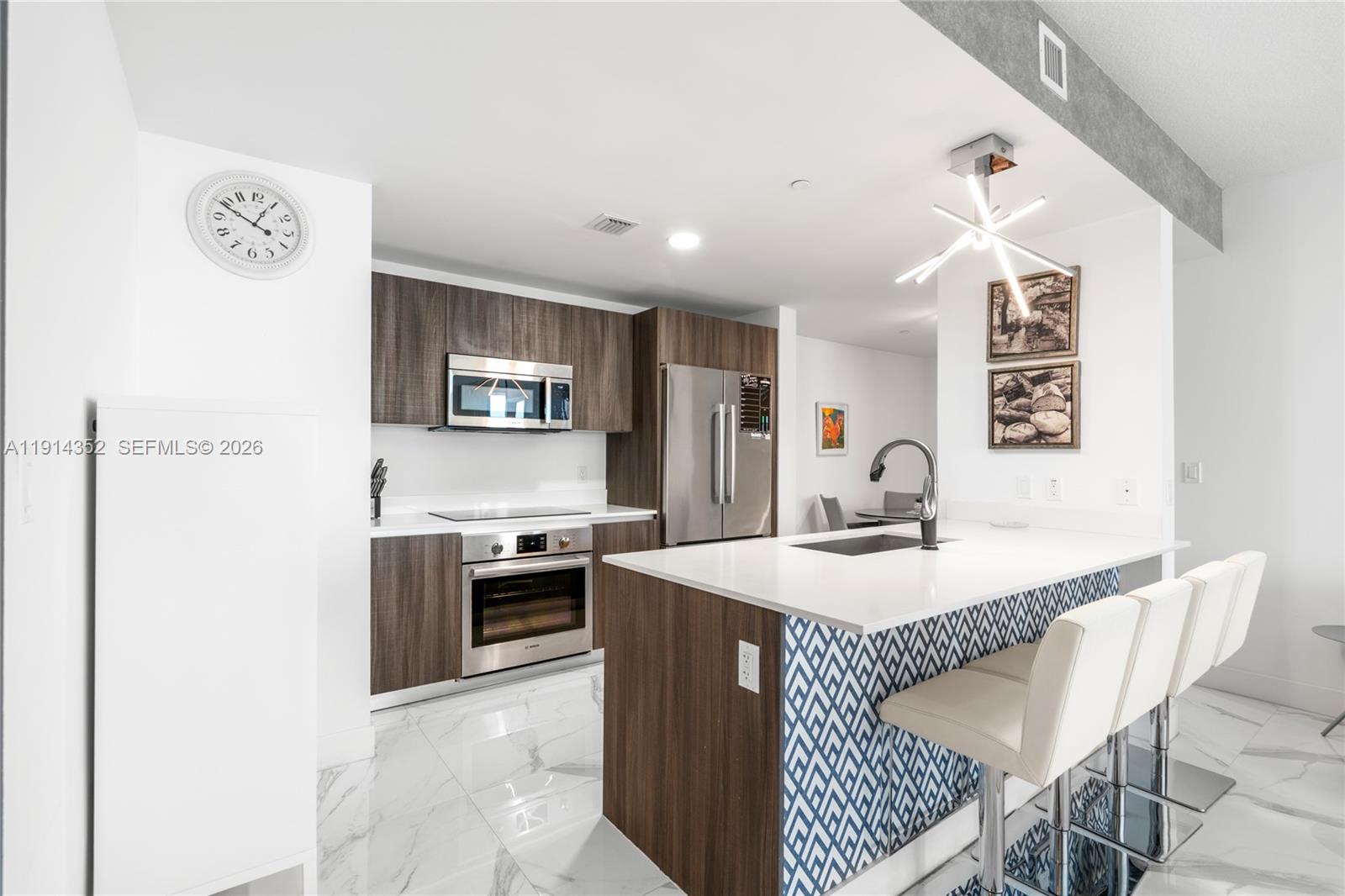 A modern kitchen features wood-grain cabinets, a white island with blue patterned tile, and marble flooring — 488 NE 18th St # 4309, Miami FL 33132, MIAMI, FL