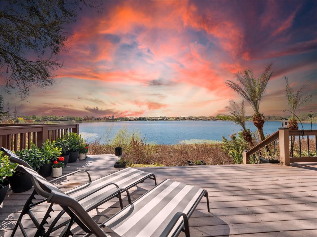 A wooden deck with lounge chairs overlooks a lake under a vibrant sunset sky — 8224 TIVOLI DRIVE, ORLANDO, FL