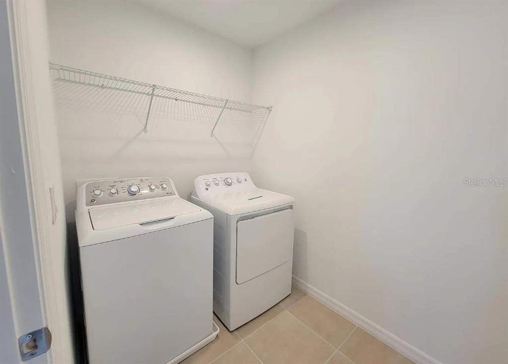 A laundry room features a white washer and dryer beneath a wire wall shelf — 216 AQUAMARINE LANE, KISSIMMEE, FL