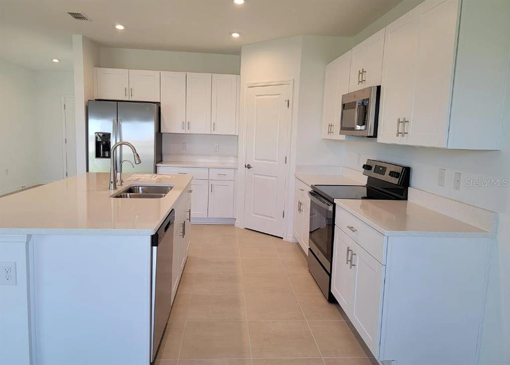 A modern kitchen features white cabinets, stainless steel appliances, and a large central island — 216 AQUAMARINE LANE, KISSIMMEE, FL