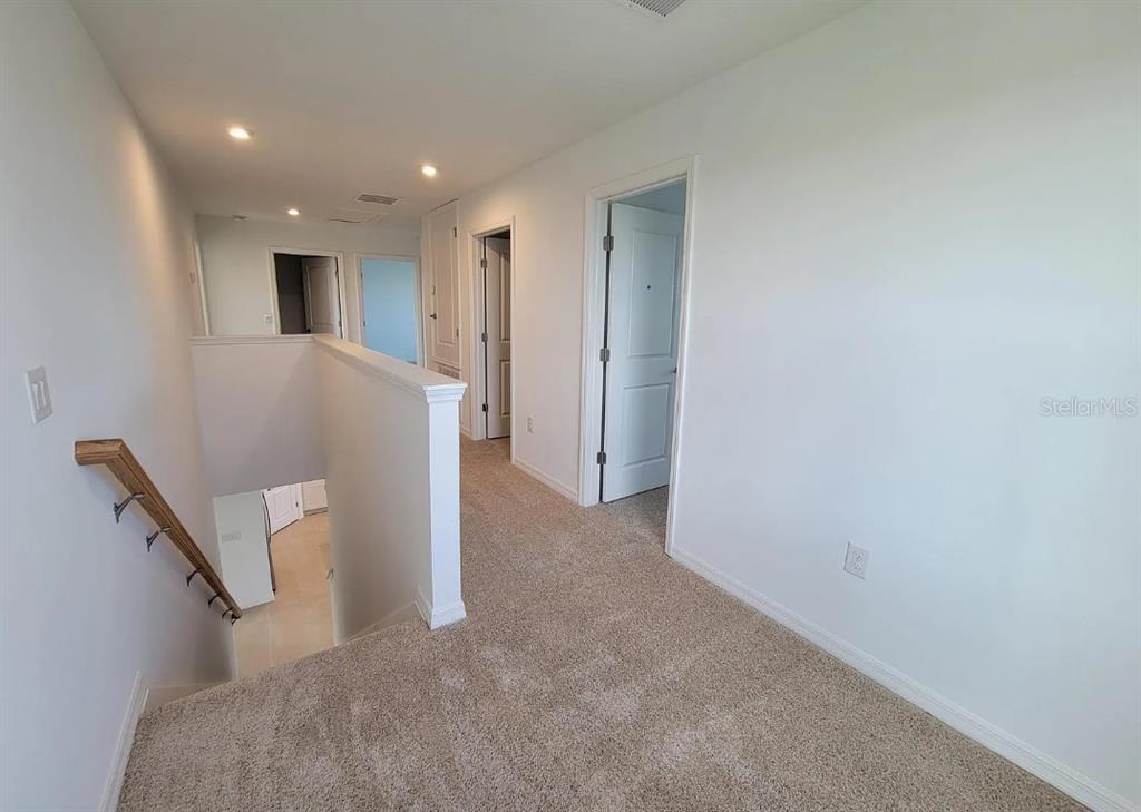 A carpeted upstairs hallway features a staircase, white walls, and several interior doors — 216 AQUAMARINE LANE, KISSIMMEE, FL