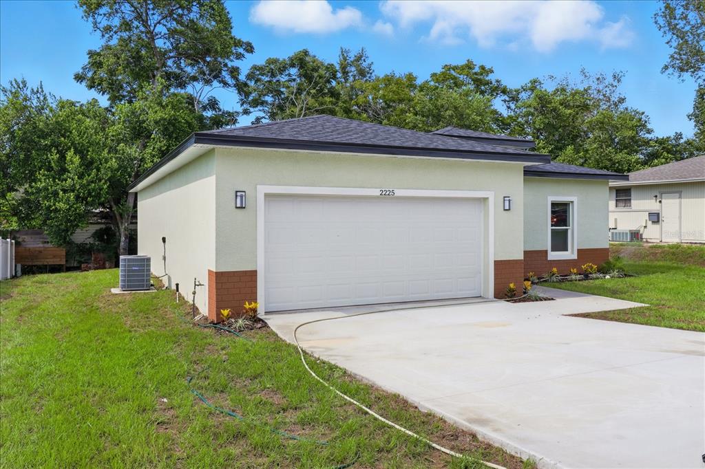A single-story house with a two-car garage, light green stucco walls, and brick accents — 2225 W HOWARD PLACE, CITRUS SPRINGS, FL