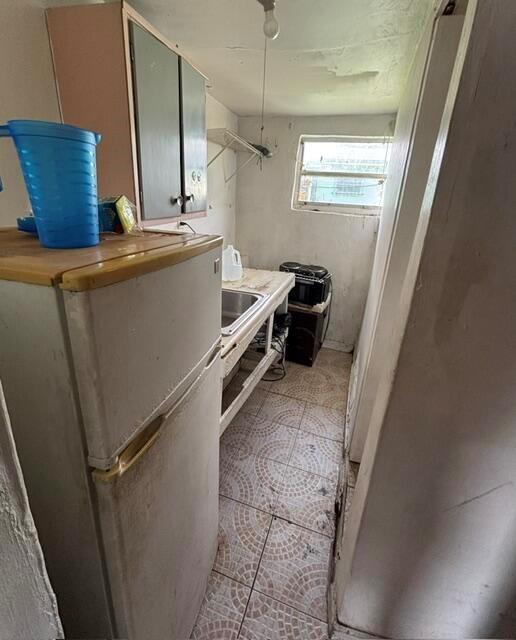 A small kitchen features a refrigerator, a sink, a window, and tiled flooring — 2451 NW 95th Terrace, Miami FL 33147, MIAMI, FL