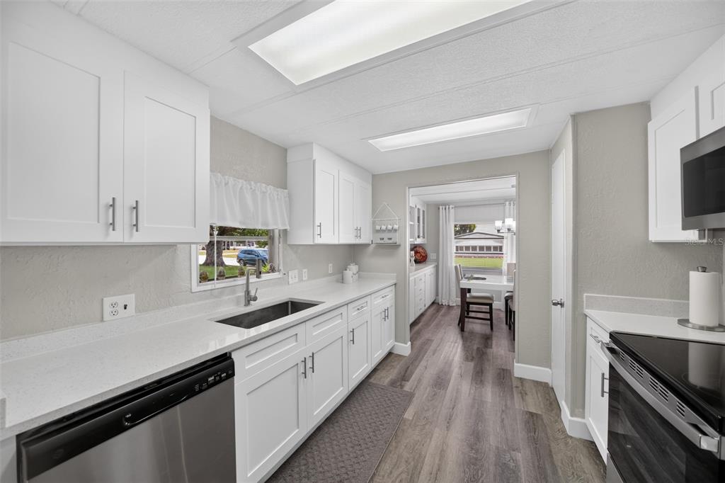 A modern kitchen features white cabinets, stainless steel appliances, and gray wood-look flooring — 3712 S CITRUS CIRCLE UNIT GE, ZELLWOOD, FL