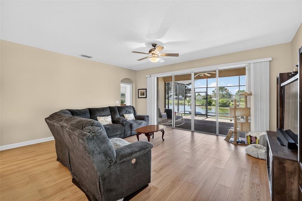 A living room with wood-look flooring, a gray sectional sofa, and sliding glass doors to a lanai — 2359 WAKEFIELD WAY, MOUNT DORA, FL