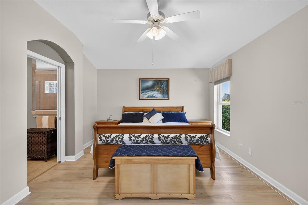 A bedroom features a wooden sleigh bed, light wood flooring, and an arched doorway — 2359 WAKEFIELD WAY, MOUNT DORA, FL