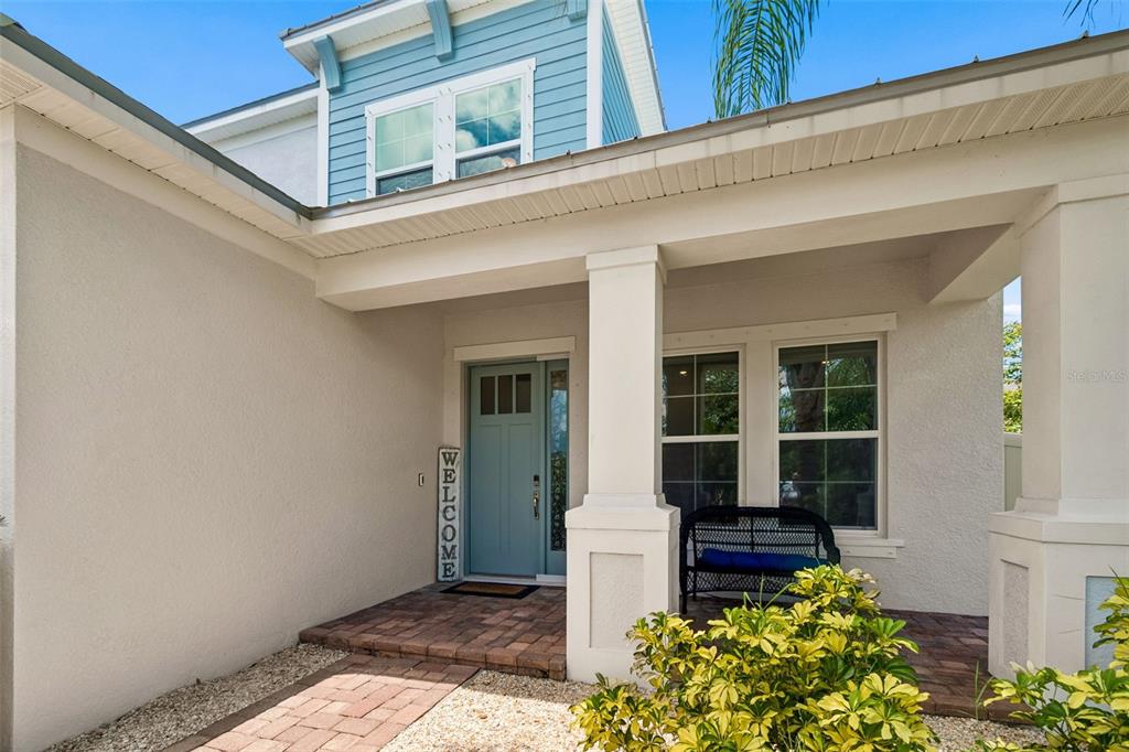 A front porch with a blue door, a welcome sign, and a black bench — 747 CAJEPUT LOOP, TARPON SPRINGS, FL