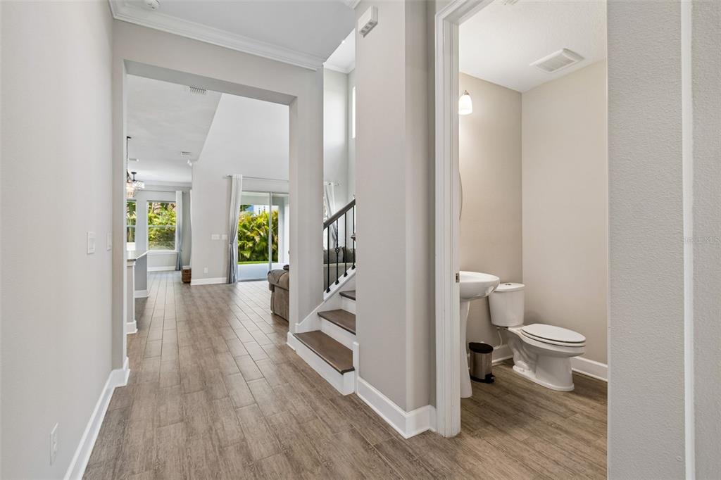 A hallway with wood-look tile flooring leads to a living area, staircase, and powder room — 747 CAJEPUT LOOP, TARPON SPRINGS, FL