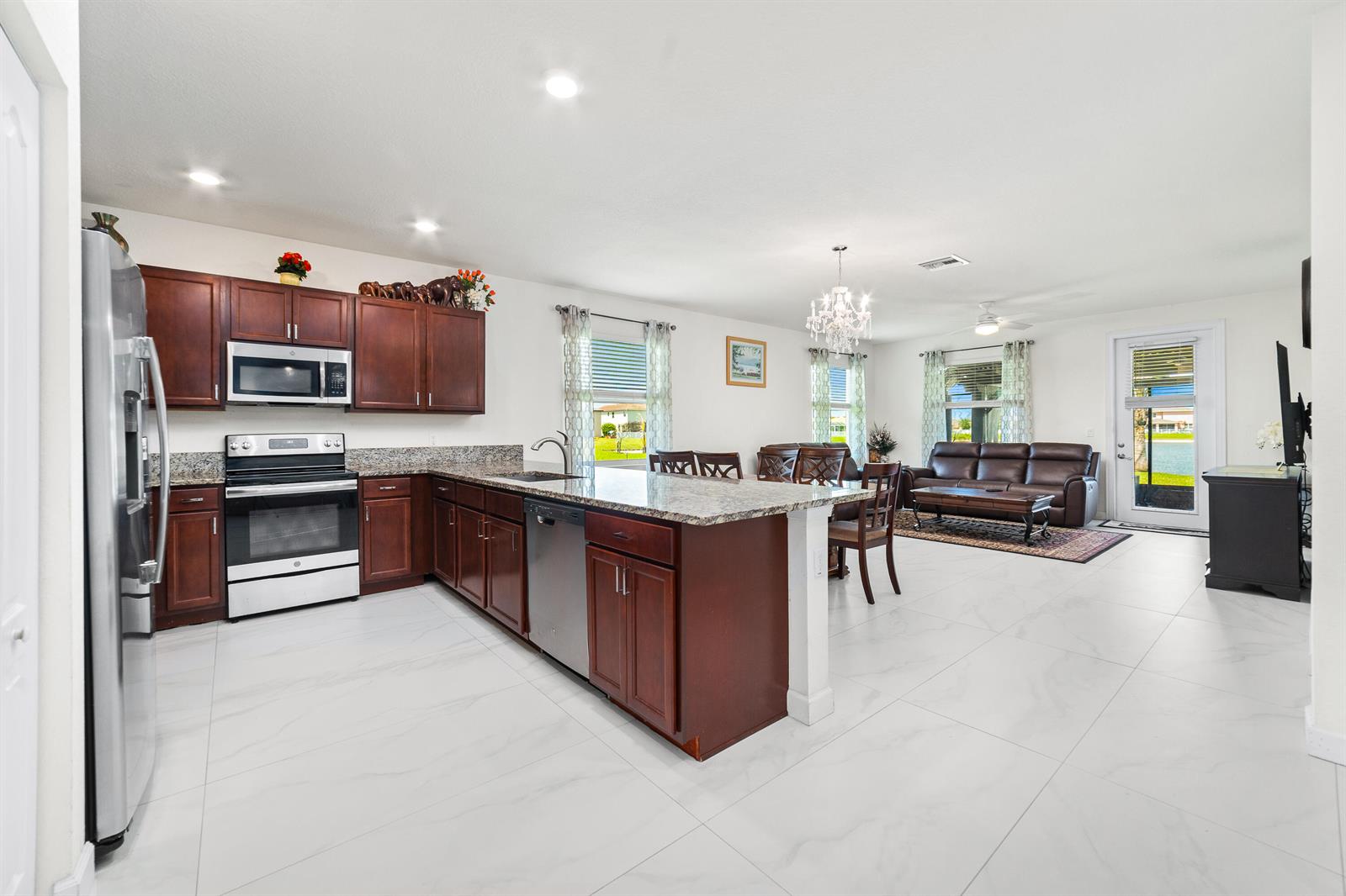 A kitchen with dark wood cabinets and granite countertops opens into a living room area — 879 Bent Creek Drive, Fort Pierce FL 34947, FORT PIERCE, FL