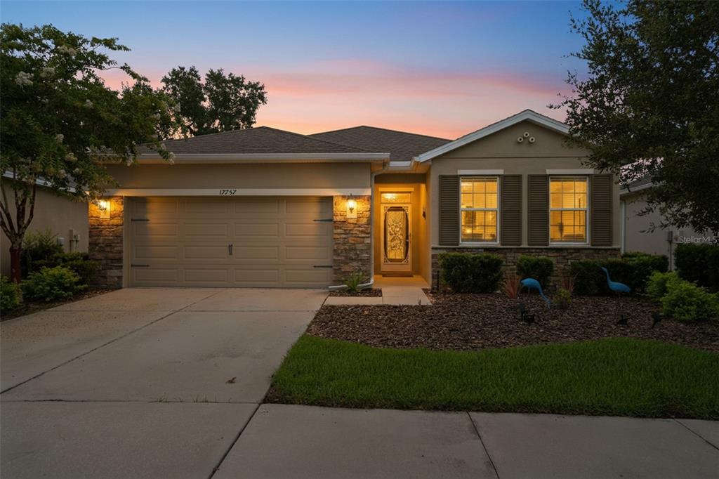A single-story house with a beige stucco exterior, stone accents, and a two-car garage — 17757 GARSALASO CIRCLE, BROOKSVILLE, FL
