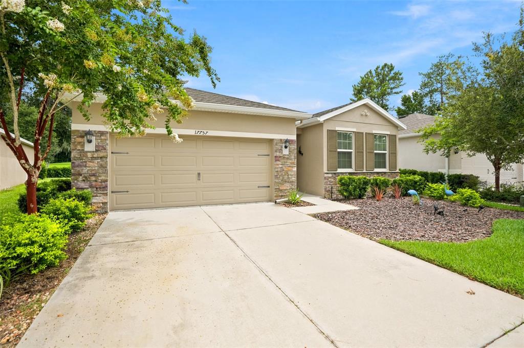 A single-story house with a beige stucco exterior, stone accents, and a two-car garage — 17757 GARSALASO CIRCLE, BROOKSVILLE, FL