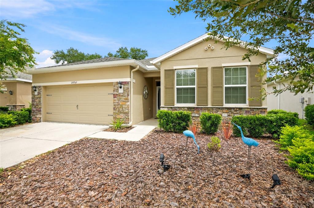 A single-story house with a tan stucco exterior, stone accents, and a two-car garage — 17757 GARSALASO CIRCLE, BROOKSVILLE, FL