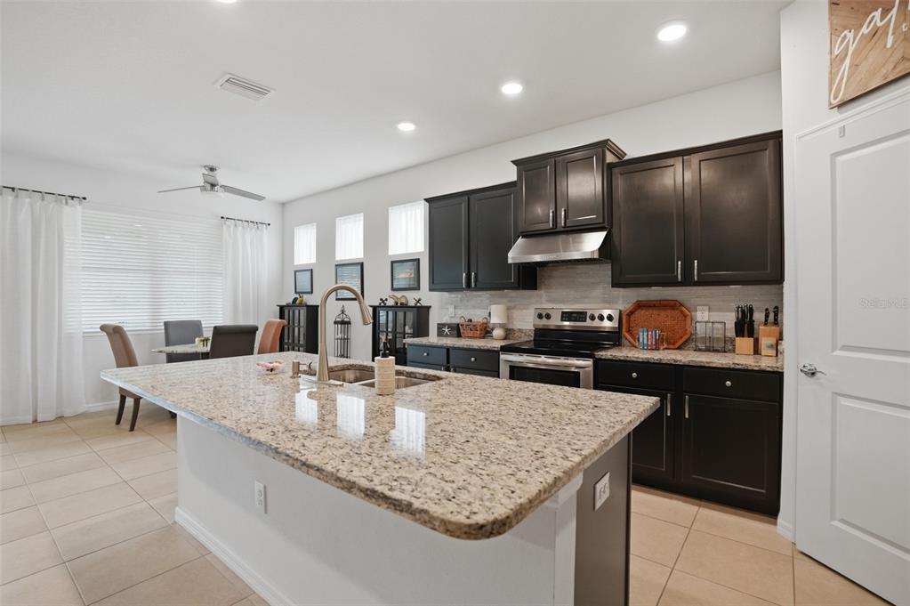 A kitchen features dark cabinets, granite countertops, a central island, and an adjacent dining area — 17757 GARSALASO CIRCLE, BROOKSVILLE, FL