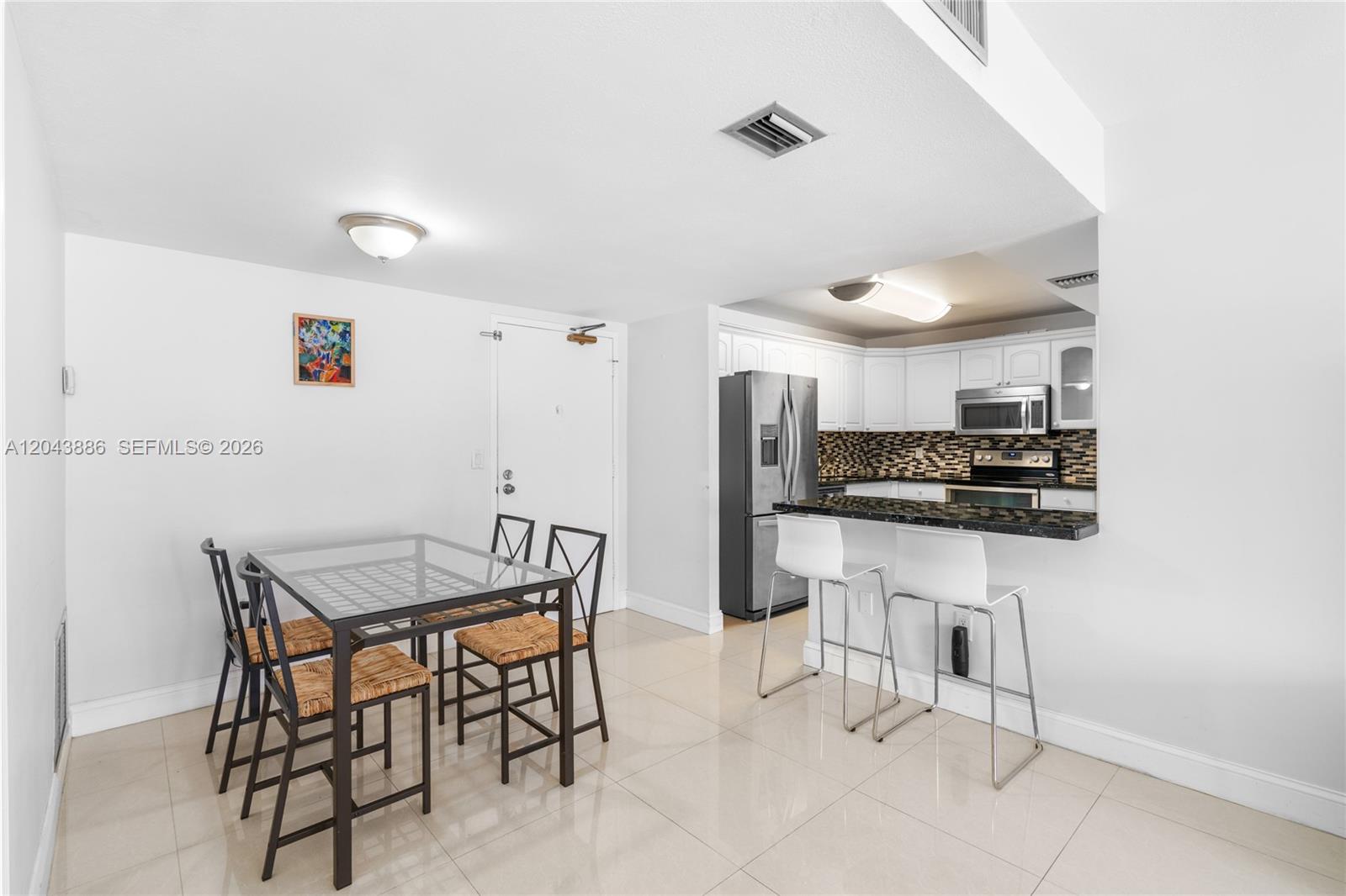 A dining area with a glass table sits adjacent to a kitchen with white cabinets — 9273 Collins Ave # 408, Surfside FL 33154, SURFSIDE, FL