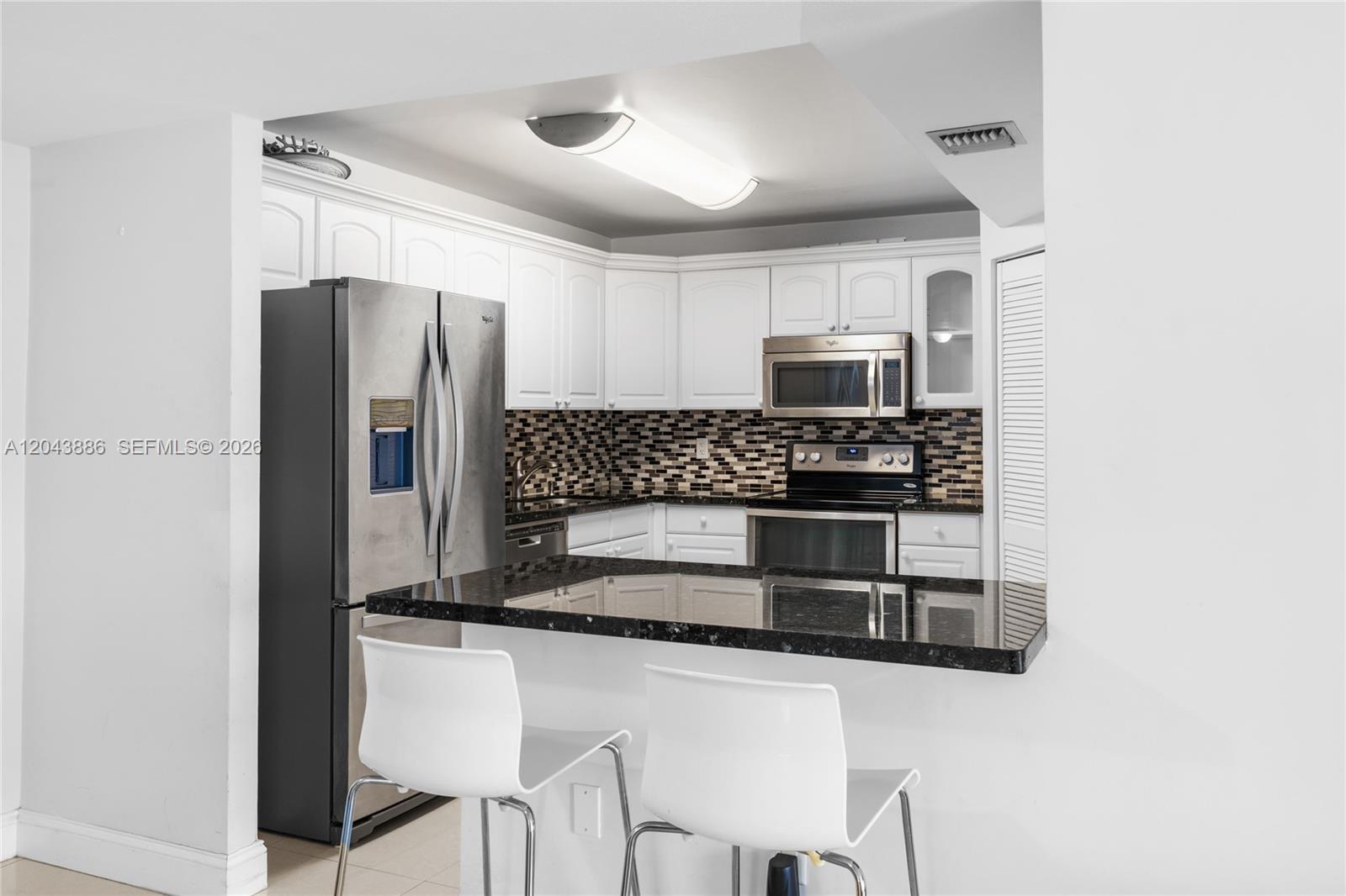 A kitchen features white cabinets, stainless steel appliances, a black granite countertop, and two chairs — 9273 Collins Ave # 408, Surfside FL 33154, SURFSIDE, FL