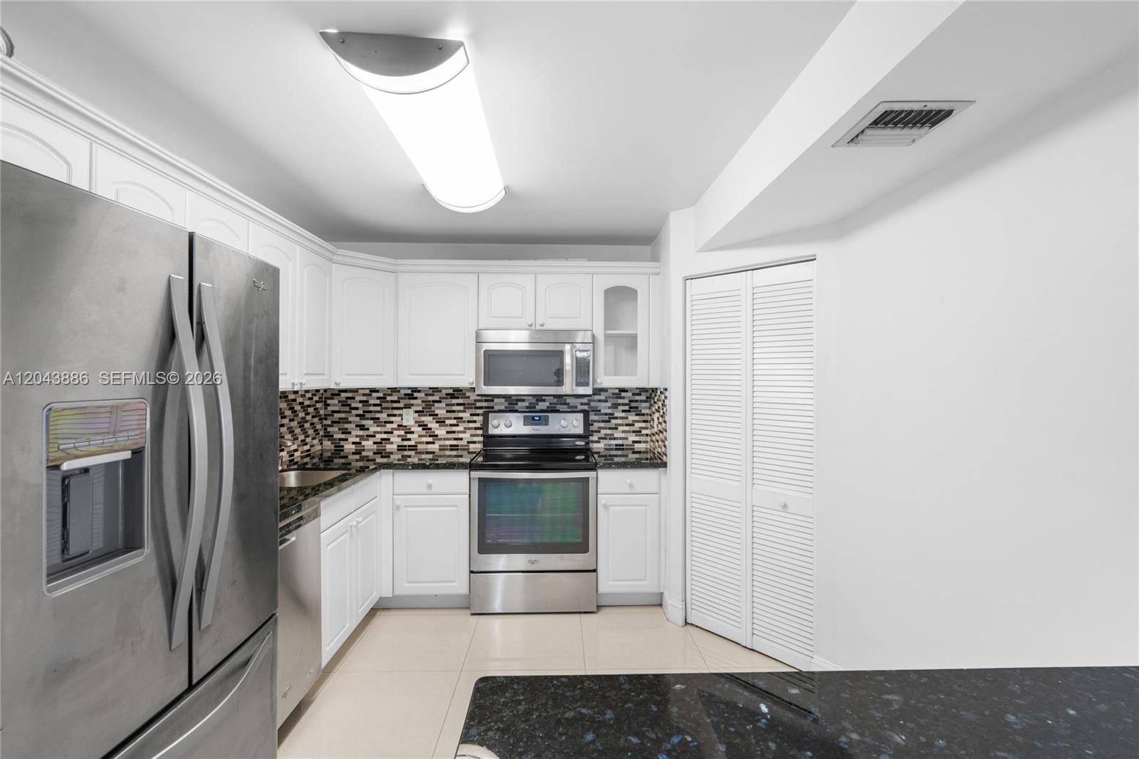 A kitchen features white cabinetry, stainless steel appliances, and a dark granite countertop — 9273 Collins Ave # 408, Surfside FL 33154, SURFSIDE, FL