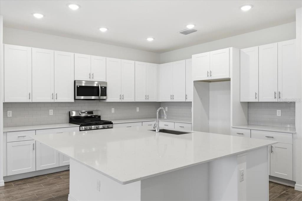 A modern kitchen features white cabinets, a large quartz island, and stainless steel appliances — 3094 WINDSWEPT WAY, WILDWOOD, FL