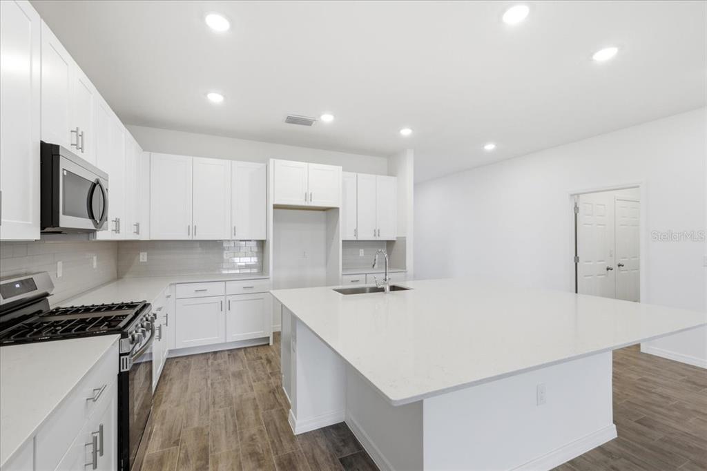 A modern kitchen features white cabinets, a large quartz island, and wood-look tile flooring — 3094 WINDSWEPT WAY, WILDWOOD, FL