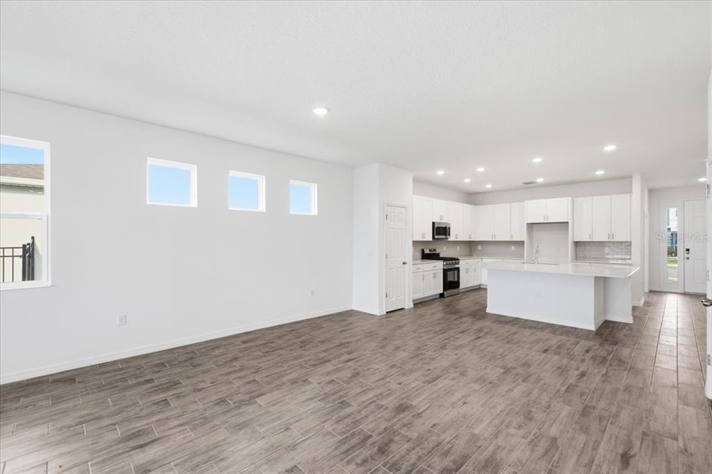 An open-concept kitchen and living area features white cabinetry, a central island, and wood-look flooring — 3094 WINDSWEPT WAY, WILDWOOD, FL