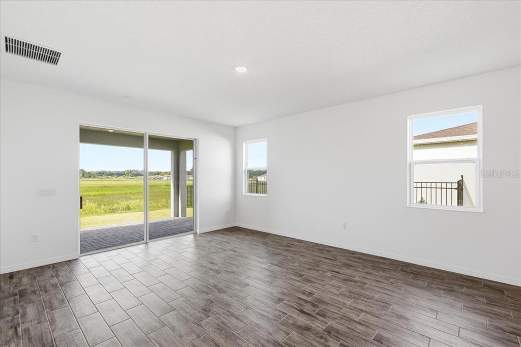An empty room features wood-look tile flooring, white walls, sliding glass doors, and two windows — 3094 WINDSWEPT WAY, WILDWOOD, FL