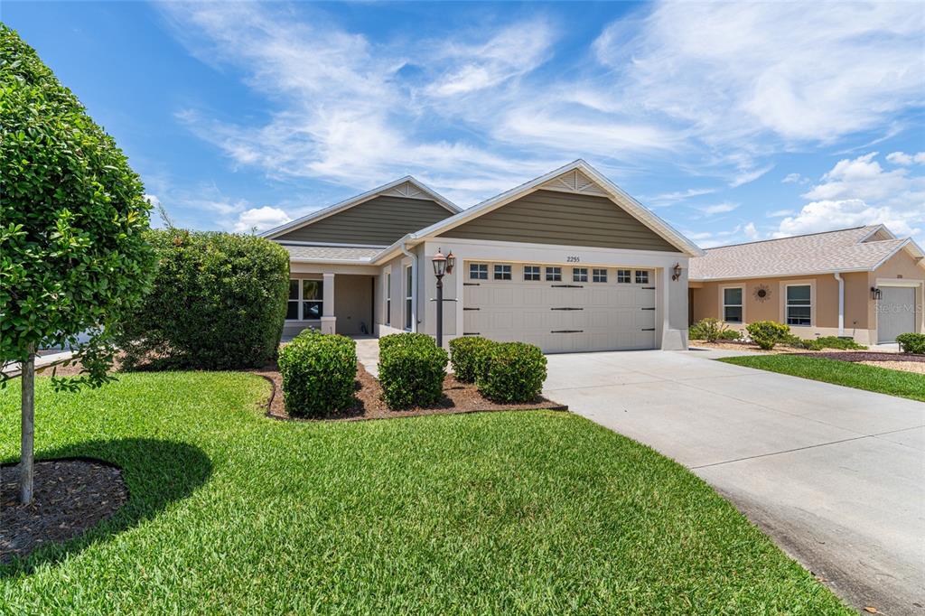 A single-story suburban house with a two-car garage, tan siding, and a manicured front lawn — 2255 PATRICIA PLACE, THE VILLAGES, FL