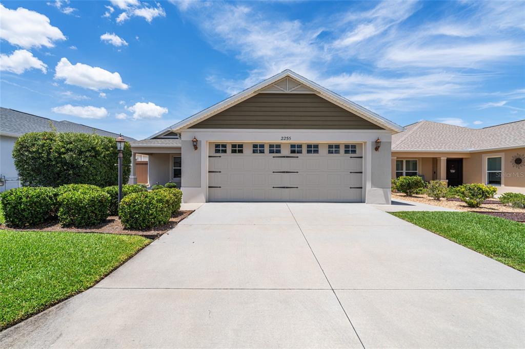 A single-story house exterior features a two-car garage, a concrete driveway, and landscaped bushes — 2255 PATRICIA PLACE, THE VILLAGES, FL
