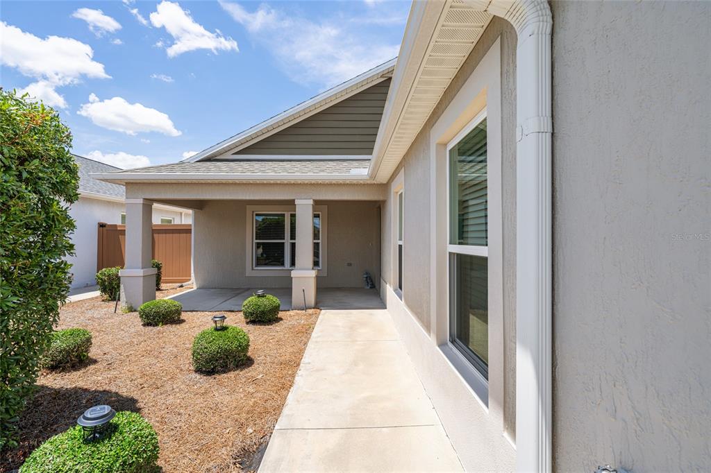 A concrete walkway leads to a covered patio beside a house with tan stucco walls — 2255 PATRICIA PLACE, THE VILLAGES, FL