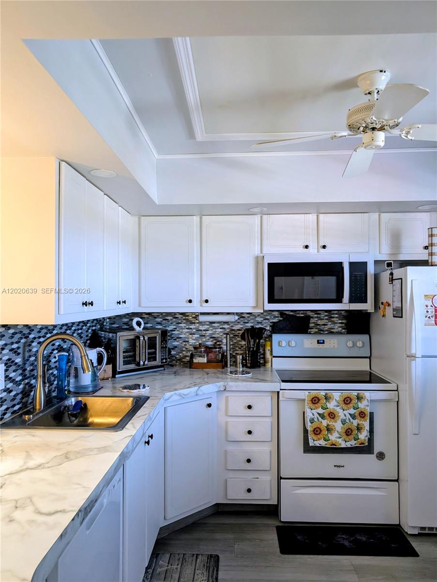 A kitchen features white cabinets, marble-patterned countertops, a mosaic backsplash, and white appliances — 130 NE 26th Ave # 4010, Boynton Beach FL 33435, BOYNTON BEACH, FL