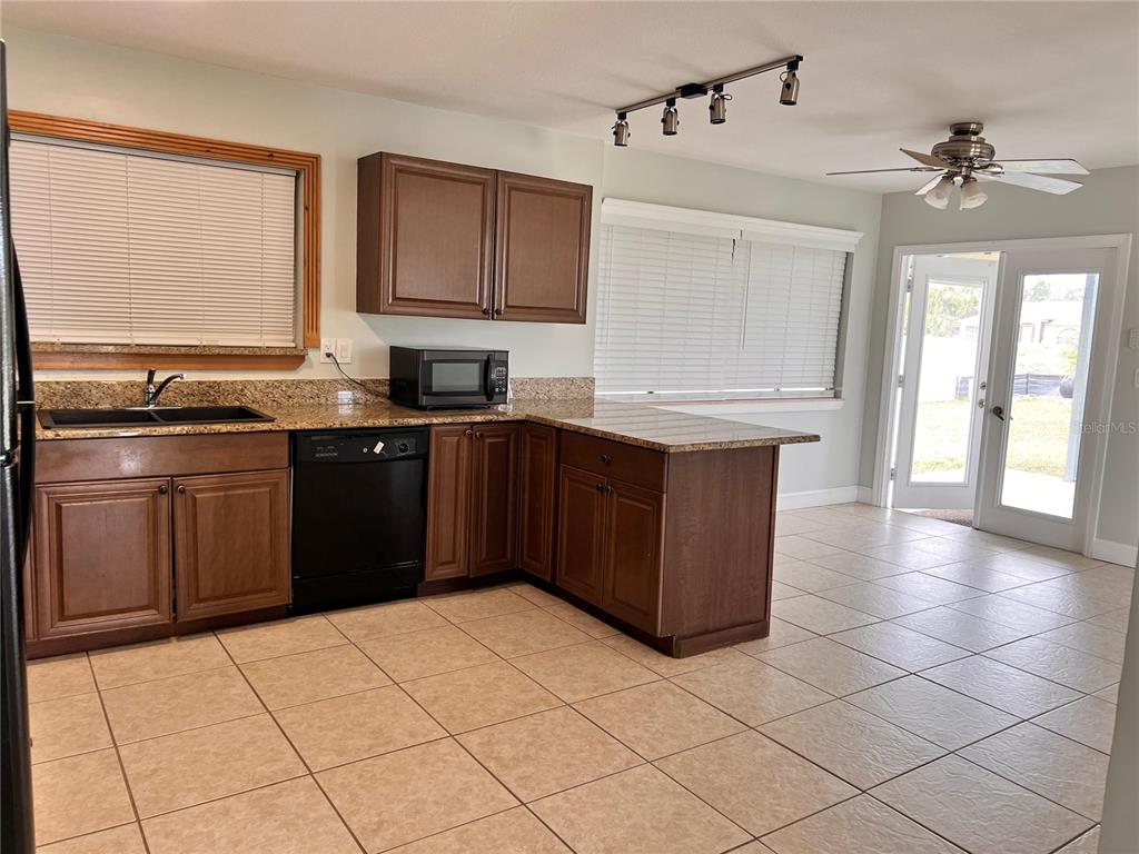 A kitchen features brown cabinets, granite countertops, a black dishwasher, and tile flooring — 1299 BIRCHCREST BOULEVARD, PORT CHARLOTTE, FL
