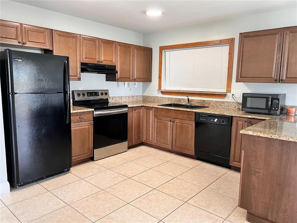 A kitchen features wood cabinets, granite countertops, tile flooring, and black appliances — 1299 BIRCHCREST BOULEVARD, PORT CHARLOTTE, FL