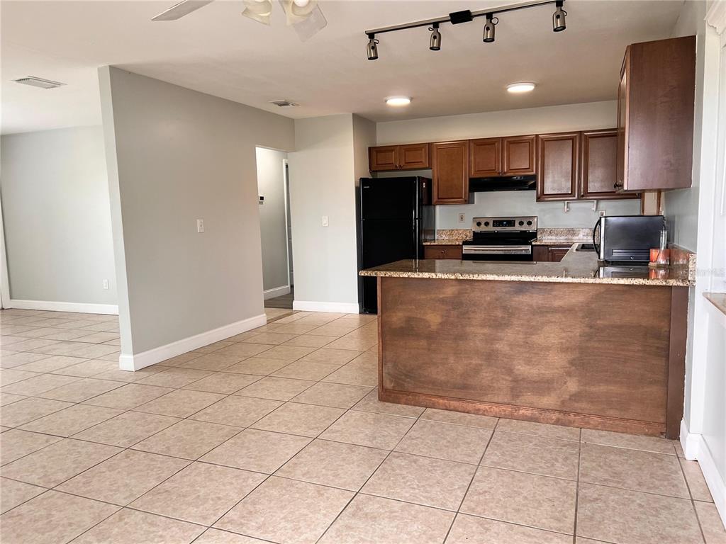 A kitchen with wood cabinets, granite countertops, and tile flooring opens to a living area — 1299 BIRCHCREST BOULEVARD, PORT CHARLOTTE, FL