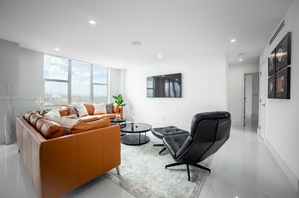 A modern living room features a tan leather sofa, black lounge chair, and floor-to-ceiling windows — 5600 Collins Ave # 14K, Miami Beach FL 33140, MIAMI BEACH, FL