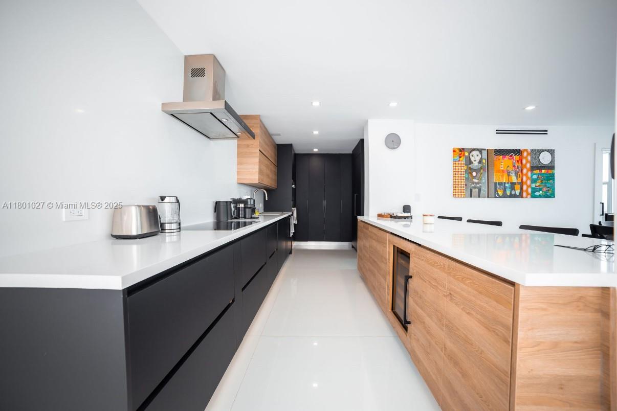 A modern kitchen features matte black cabinetry, wood-toned accents, and white countertops — 5600 Collins Ave # 14K, Miami Beach FL 33140, MIAMI BEACH, FL