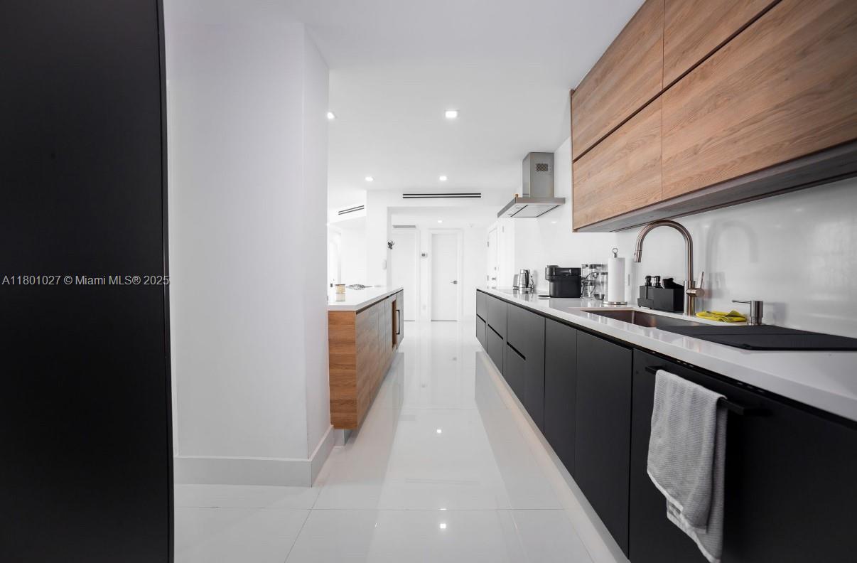 A modern kitchen features matte black lower cabinets, wood-toned upper cabinets, and white countertops — 5600 Collins Ave # 14K, Miami Beach FL 33140, MIAMI BEACH, FL