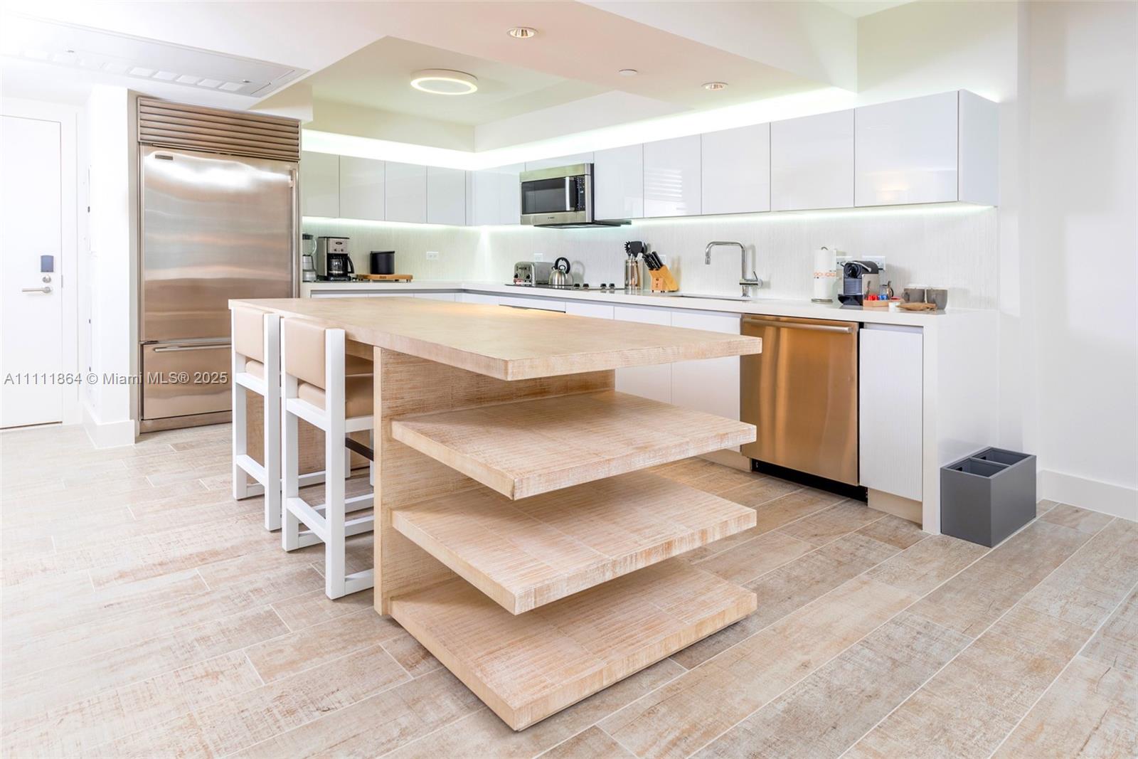 A modern kitchen features white cabinetry, stainless steel appliances, and a wooden island with shelving — 102 24th St # 906, Miami Beach FL 33139, MIAMI BEACH, FL