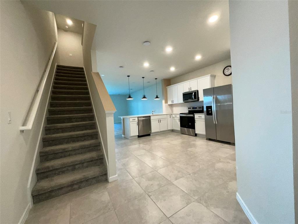 A staircase with carpeted steps leads up next to an open-concept kitchen with stainless appliances — 2619 WINSOME WAY, DAVENPORT, FL