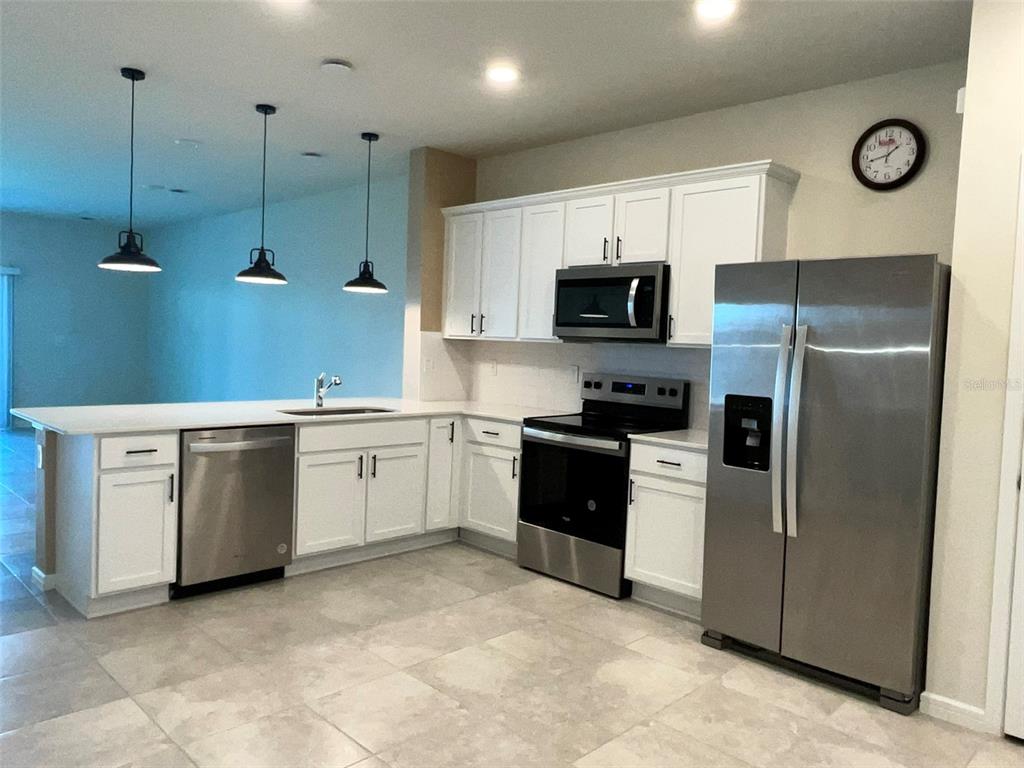 A modern kitchen features white cabinetry, stainless steel appliances, and a breakfast bar with pendants — 2619 WINSOME WAY, DAVENPORT, FL