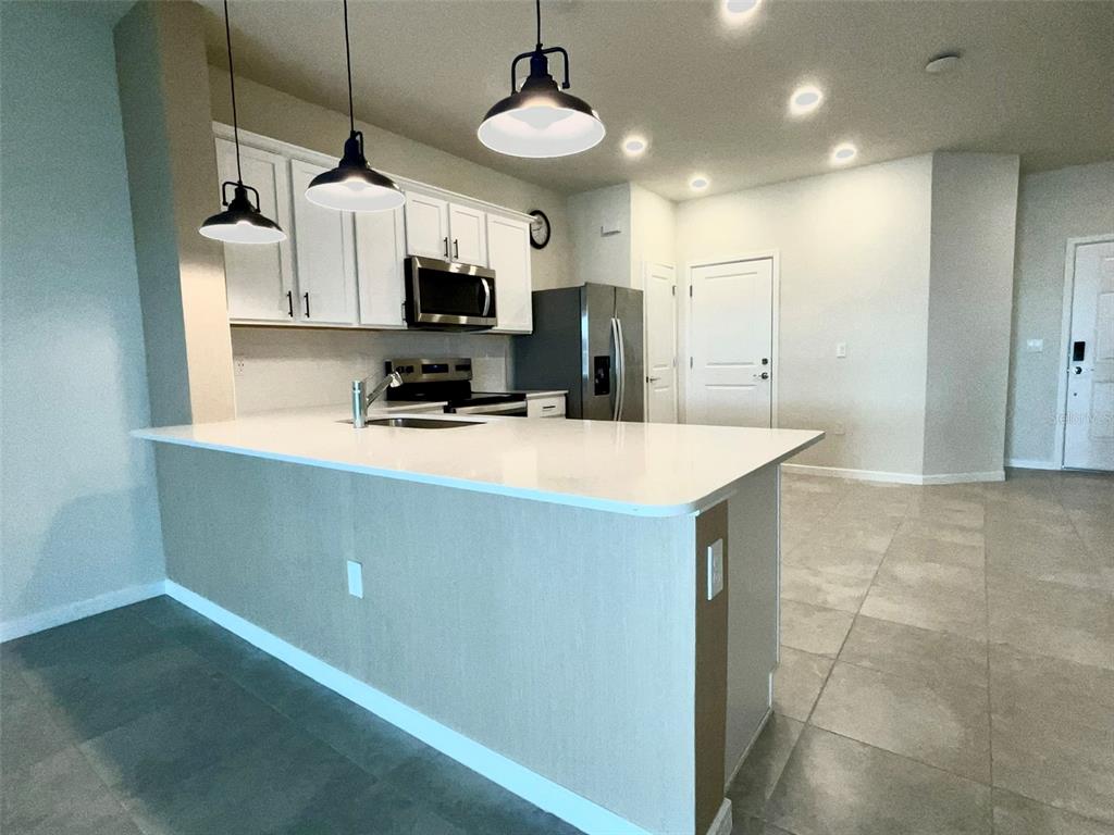 A modern kitchen features white cabinets, stainless steel appliances, and a large quartz-topped island — 2619 WINSOME WAY, DAVENPORT, FL