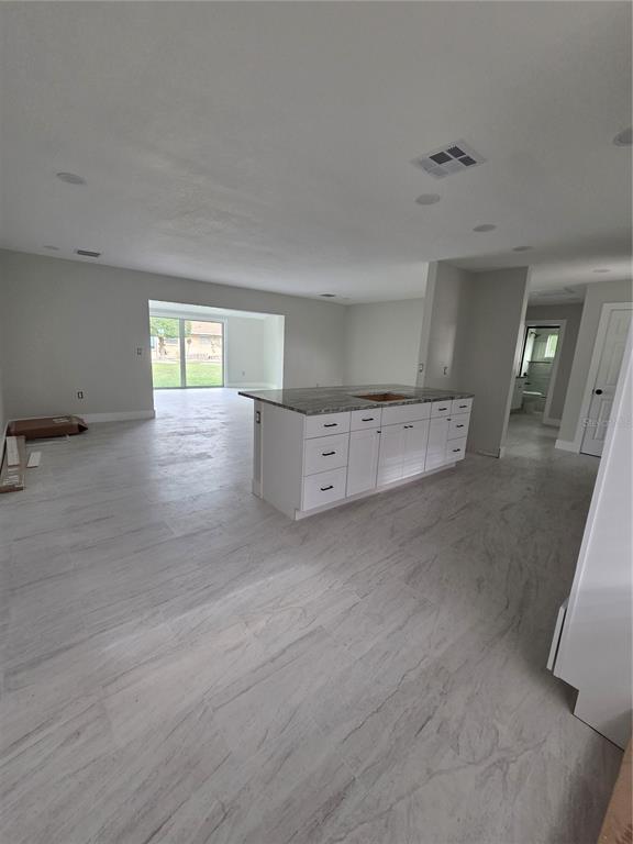 A kitchen island with a stone countertop sits in an open-concept room with light flooring — 1238 VALLEY FORGE BOULEVARD, SUN CITY CENTER, FL