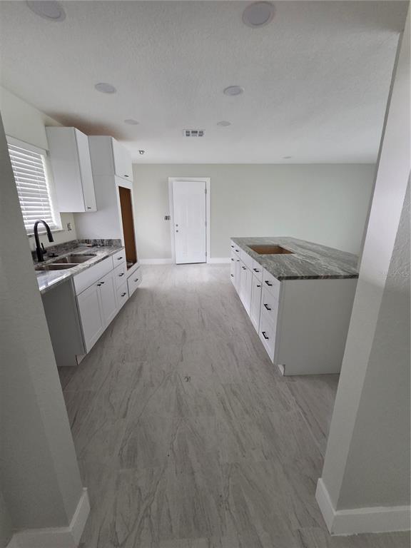 A kitchen features white cabinets, stone countertops, a central island, and light-colored tile flooring — 1238 VALLEY FORGE BOULEVARD, SUN CITY CENTER, FL