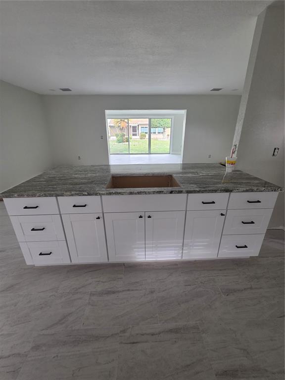 A kitchen island with white cabinets and a stone countertop sits in a room with tile — 1238 VALLEY FORGE BOULEVARD, SUN CITY CENTER, FL