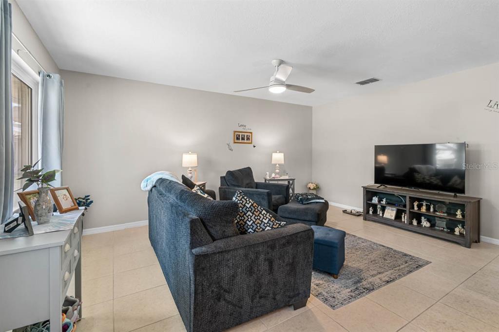 A living room features a dark sofa, a television on a console, and tile flooring — 1906 CANTERBURY LANE UNIT 26, SUN CITY CENTER, FL