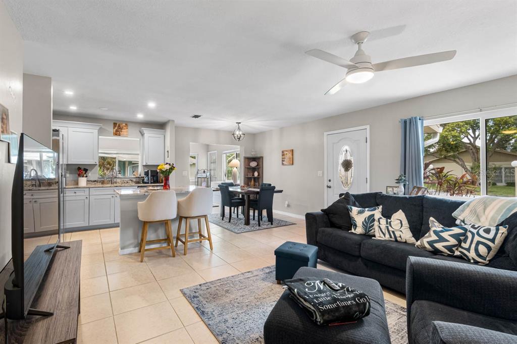 An open-concept living room and kitchen featuring light gray cabinets, tile flooring, and a ceiling fan — 1906 CANTERBURY LANE UNIT 26, SUN CITY CENTER, FL