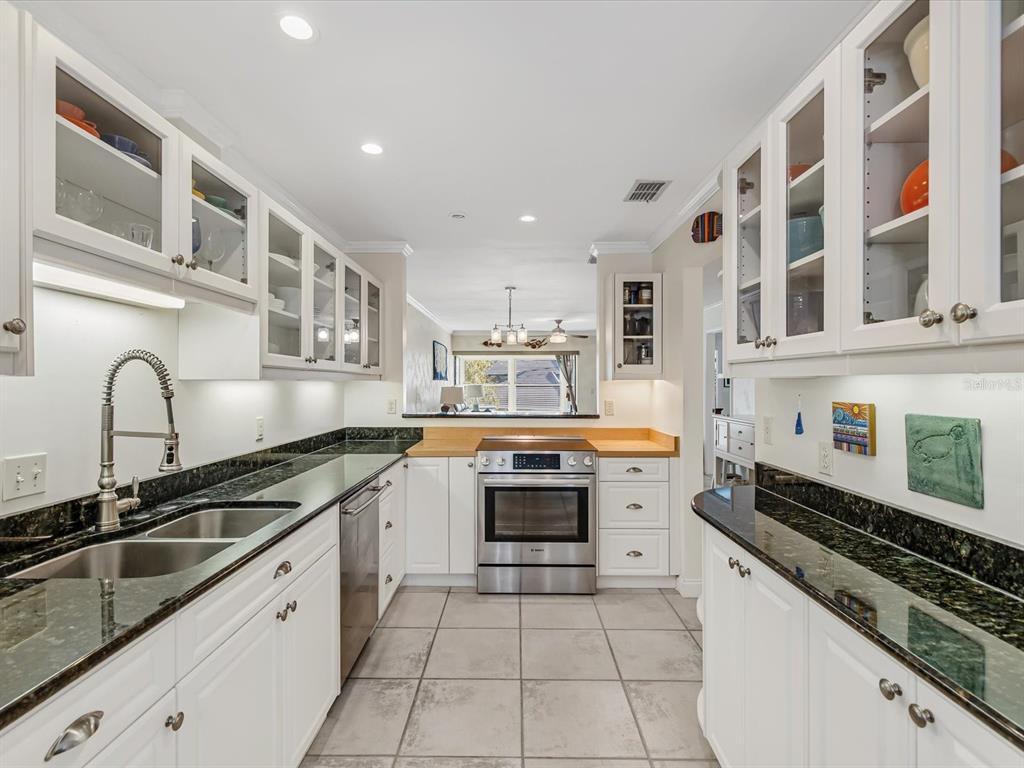 A galley kitchen features white cabinets, dark granite countertops, stainless steel appliances, and tile flooring — 413 S BAYSHORE BOULEVARD UNIT 4, SAFETY HARBOR, FL