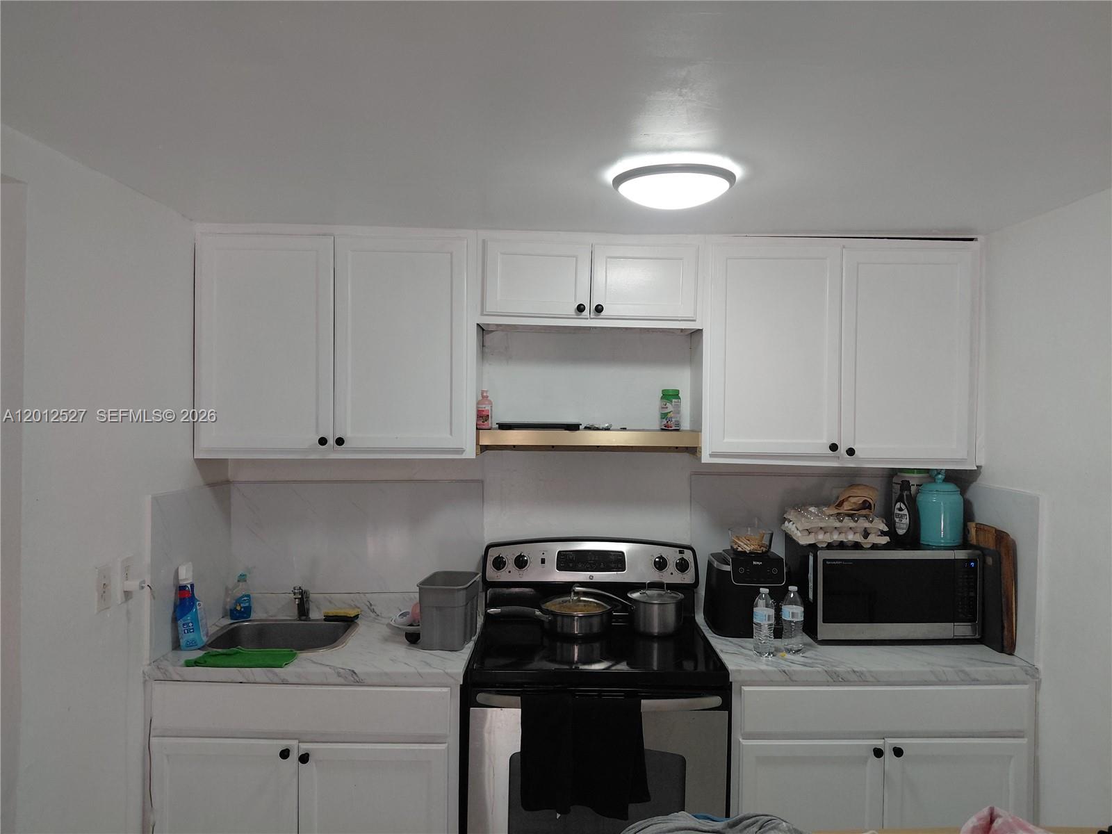 A kitchen features white cabinets, a black stove, a stainless steel sink, and marble-patterned countertops — 2140 NW 1st Ter, Miami FL 33125, MIAMI, FL